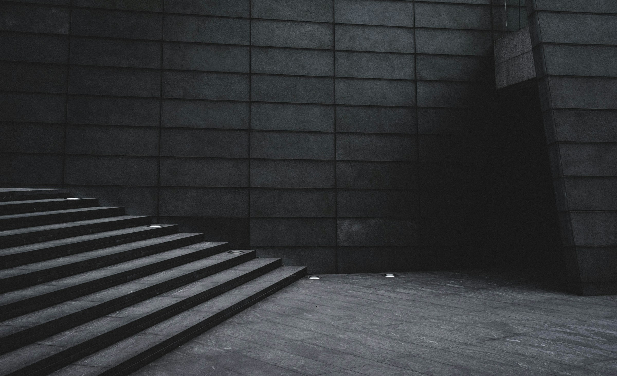 Dark stone staircase rising beside a tiled concrete wall